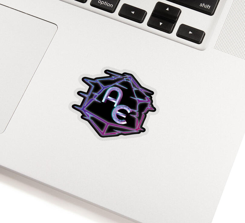 Listing photo of a die-cut sticker of the AEA glitched-d20 logo stuck to the surface of a silver/white laptop.